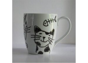 A white mug with black cat and fish designs on it.