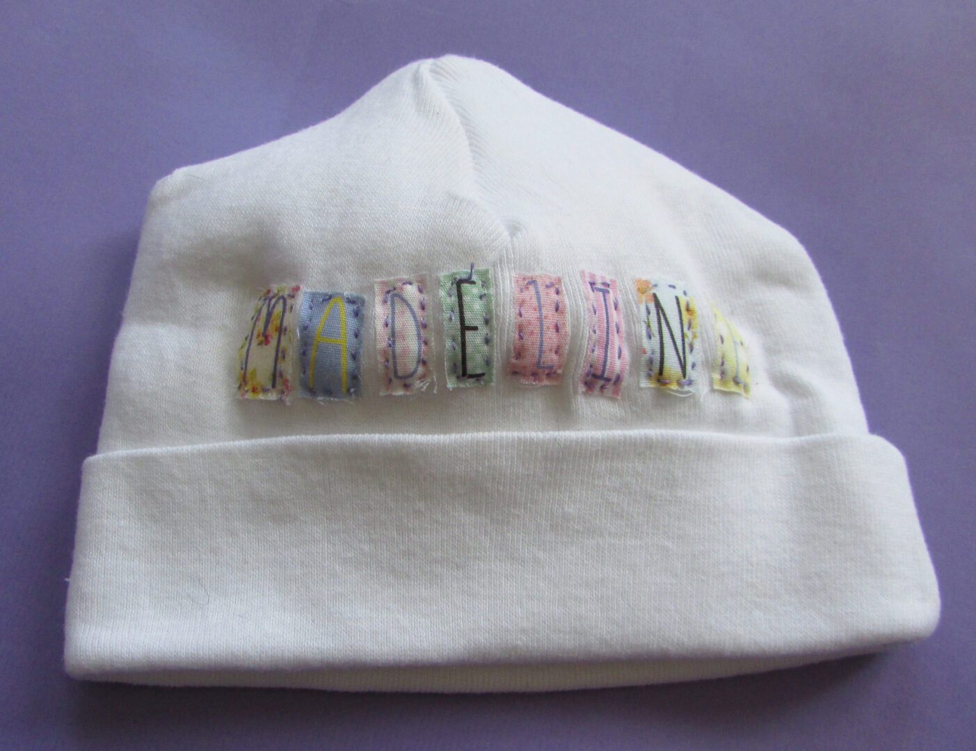 A white Personalized Infant Knit Cap with the word 'moon' embroidered on it.